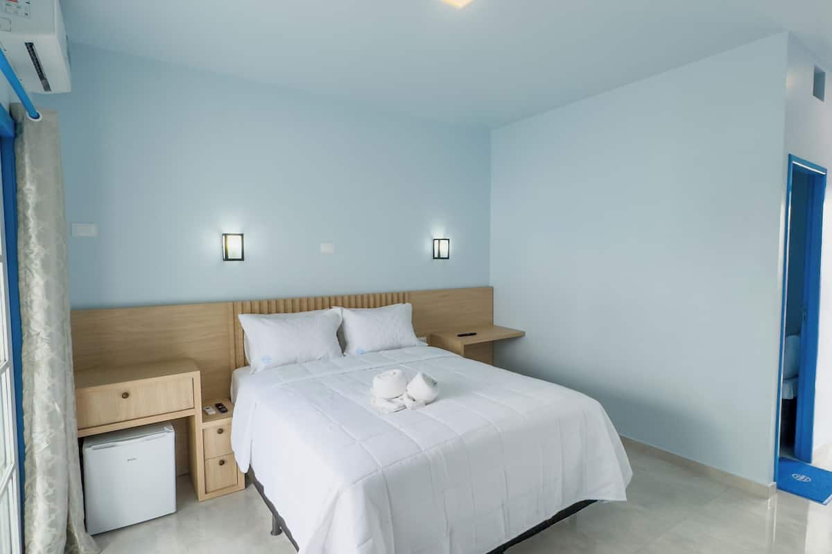 Ein Hotelzimmer mit Bett, Nachttischen, einer Wand-Klimaanlage und einer Tür.