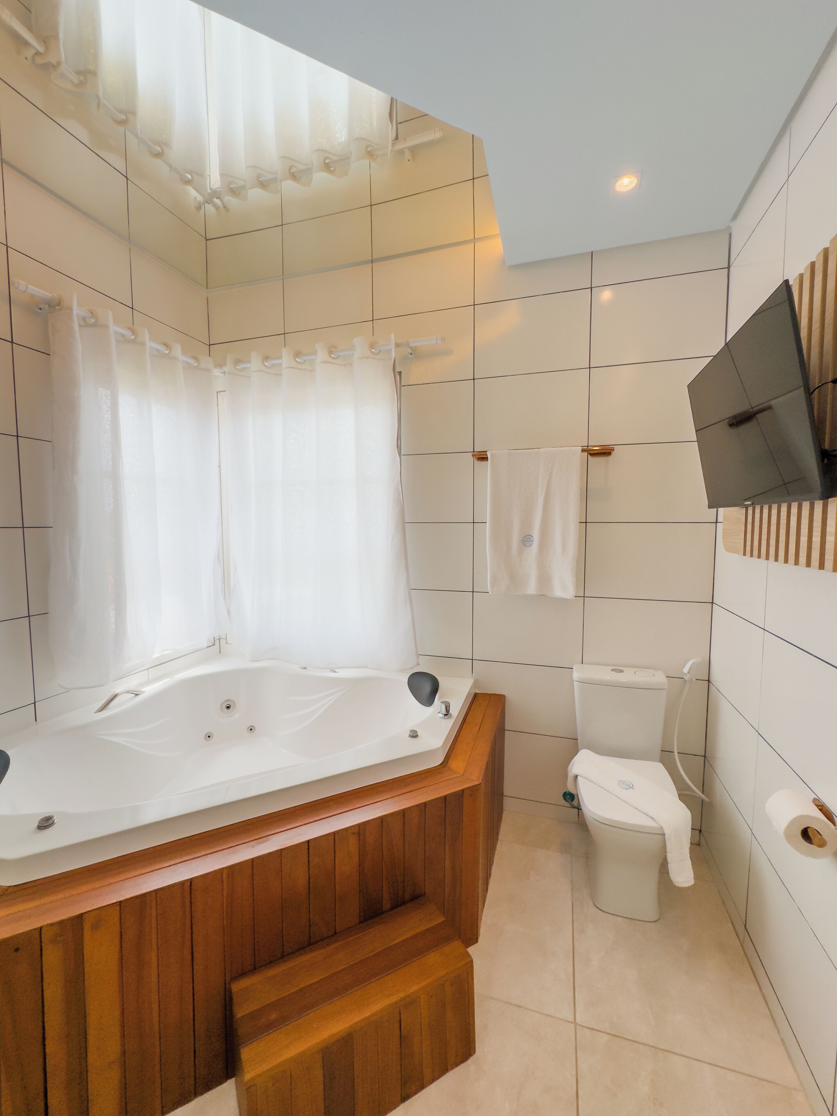 A modern bathroom with a wooden bathtub, a toilet, and a shower curtain.