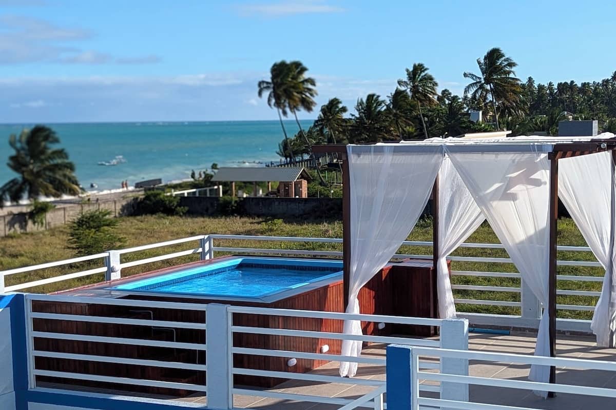 Ein Poolbereich auf dem Dach mit freiem Blick auf das Meer, umgeben von Palmen und einer weißen Markise.