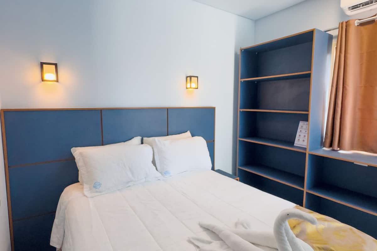 Ein Hotelzimmer mit einem Bett, zwei Wandleuchten, einem blauen Kopfteil, einem braunen Vorhang und einer Schrankwand.