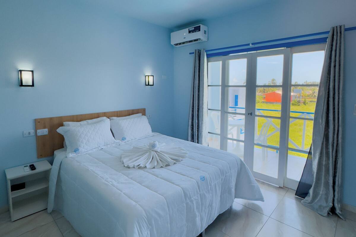 Ein Schlafzimmer mit Bett, Nachttischen, einer Klimaanlage und Blick durch eine Glastür.