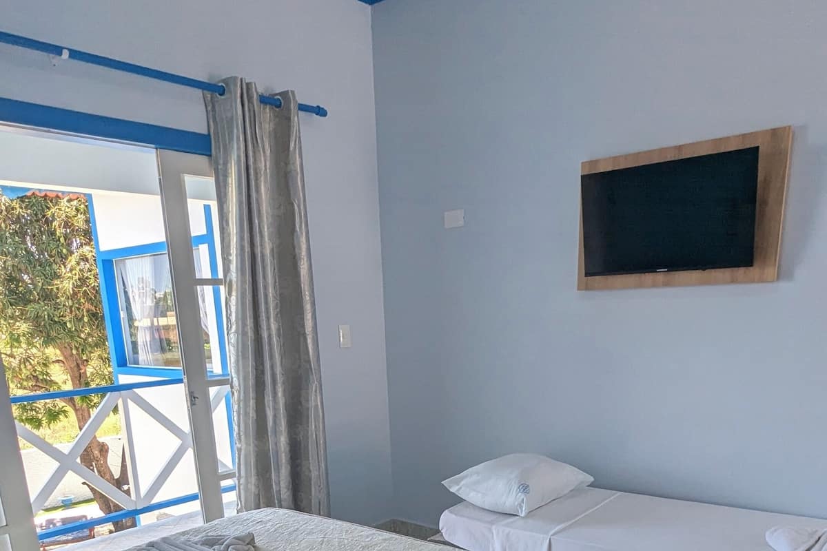 Ein Hotelzimmer mit einem großen Bett, einem kleineren Bett, einem Wandfernseher und Blick ins Freie.