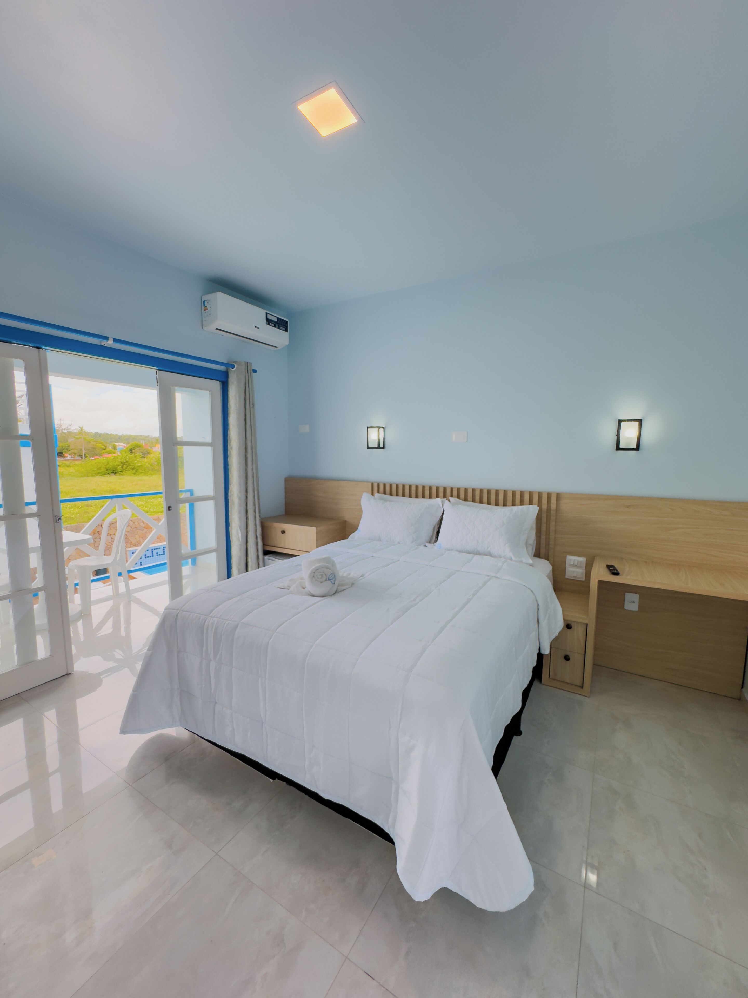 Un dormitorio con cama, mesitas de noche, un ventanal con vistas y un equipo de aire acondicionado.