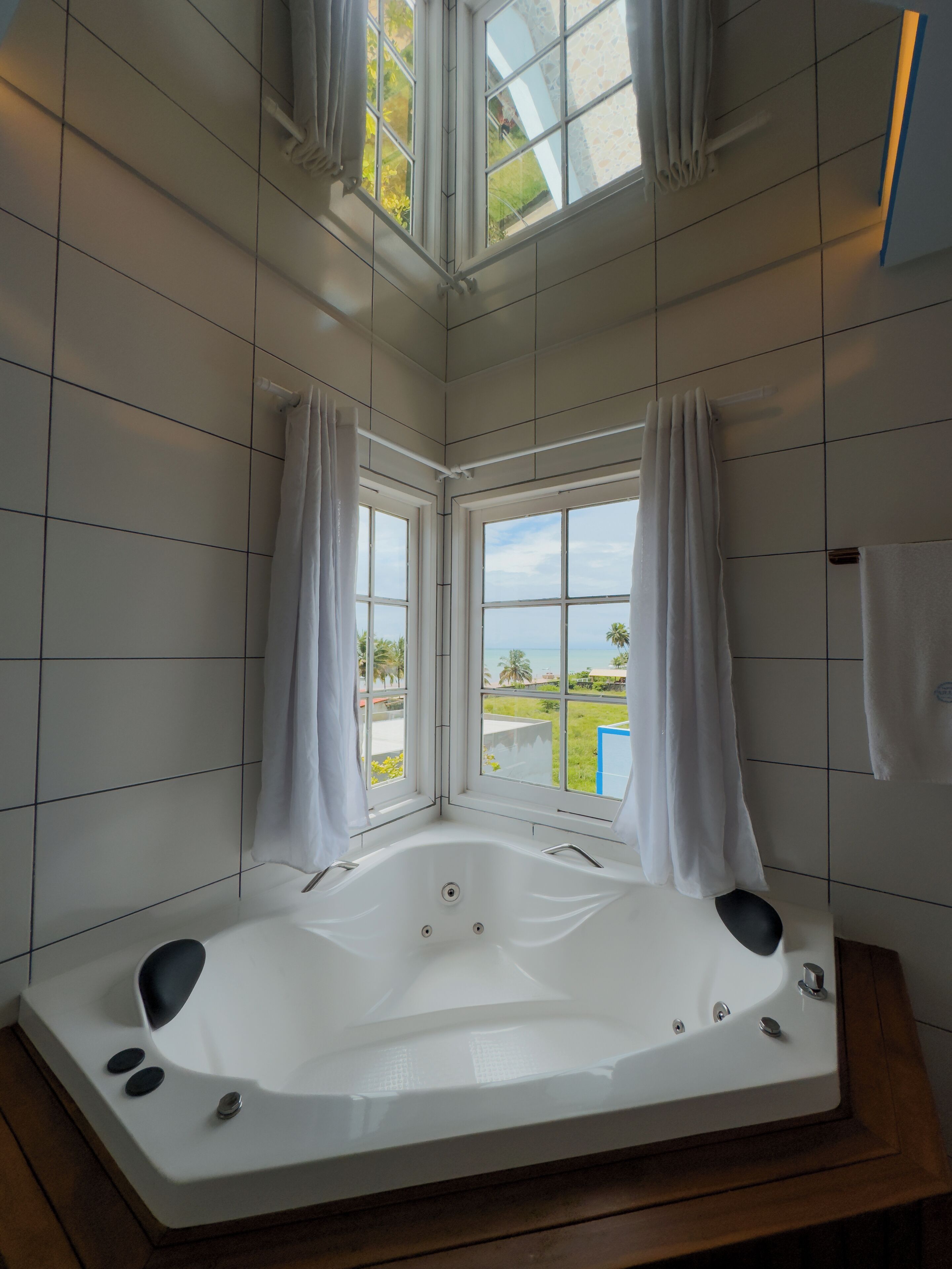 Un baño moderno con una bañera grande, paredes de azulejos blancos y vistas al océano a través de amplias ventanas.