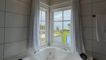 Un baño moderno con una bañera grande, paredes de azulejos blancos y vistas al océano a través de amplias ventanas.