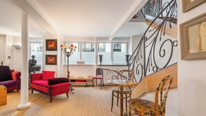 Een ruime woonkamer met een rode bank, een houten eettafel en een trap met decoratieve metalen leuningen.