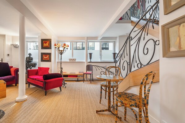 A spacious living area with a red sofa, a wooden dining table, and a staircase with ornate metal railings.