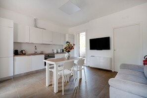 A modern kitchen with white cabinets, a dining table with chairs, a vase with flowers, and a flat-screen TV mounted on the wall.