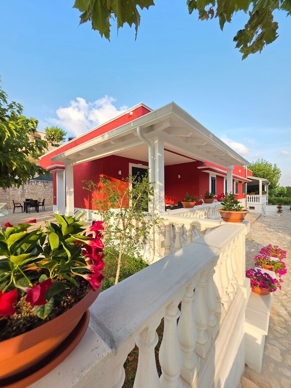 A red building with a covered patio area, stone walls, and potted plants.