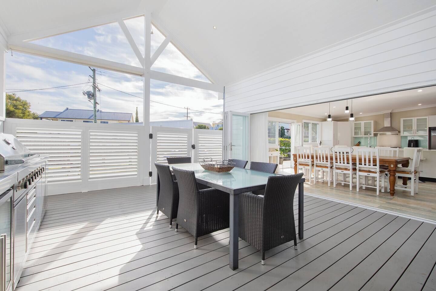 Enjoy relaxed alfresco meals on the expansive covered deck, where a six-seater dining table sits beside a full outdoor kitchen complete with built-in BBQ, sink, and generous counter space.