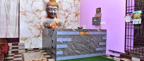 Un espace d’accueil avec un mur en marbre, une statue de Bouddha, un comptoir d’accueil et un sol à carreaux.