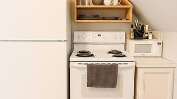 A kitchen with a white refrigerator, stove, microwave, and a wooden shelf above the stove.