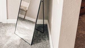 Un rincón de una habitación con un espejo de pie, un armario de madera y una pequeña mesa con un farol.