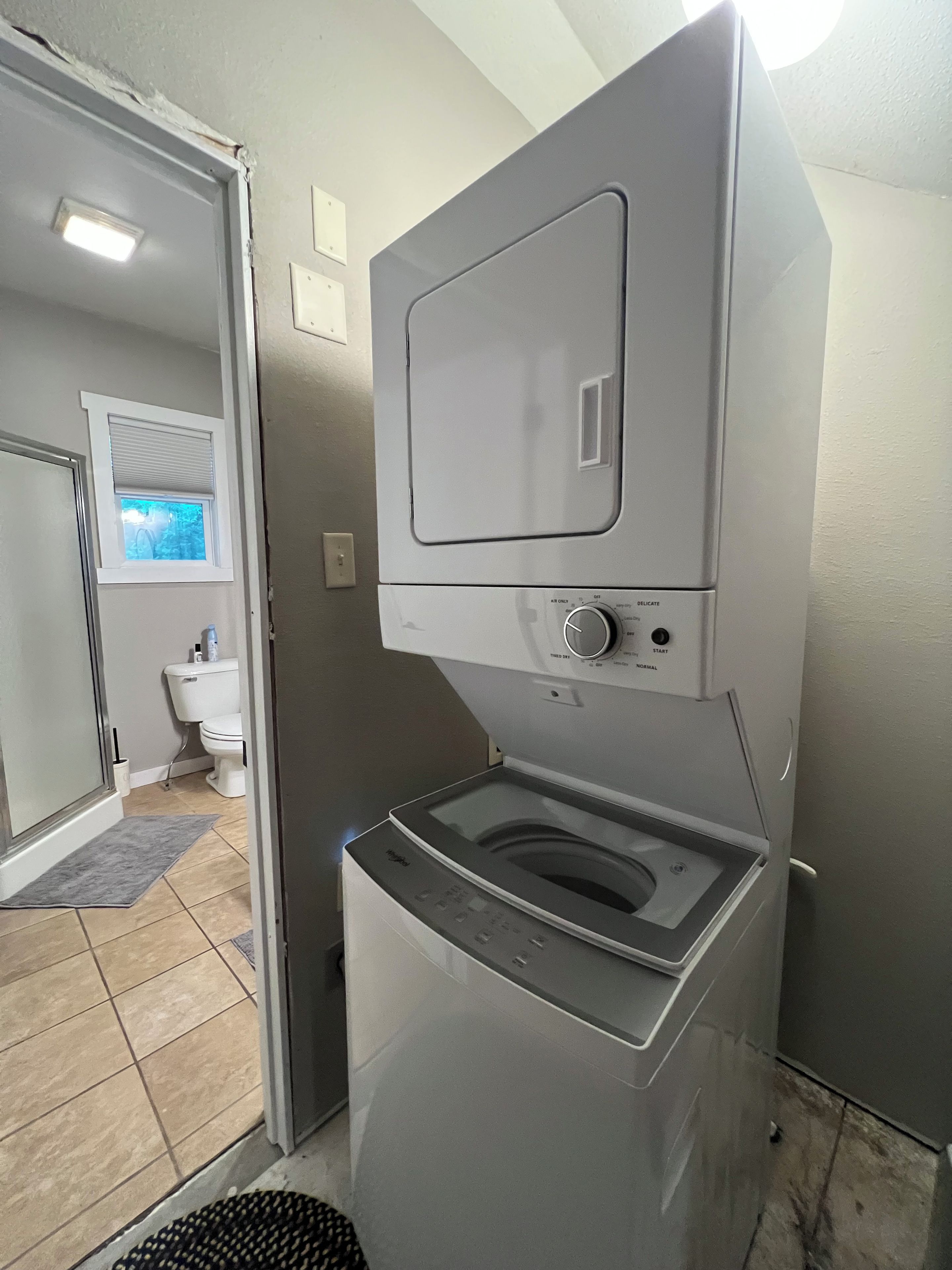 Ein kleiner Hauswirtschaftsraum mit einer Waschmaschine und einem Trockner mit Frontlader, einem kleinen Fenster und einer Tür zu einem Badezimmer.