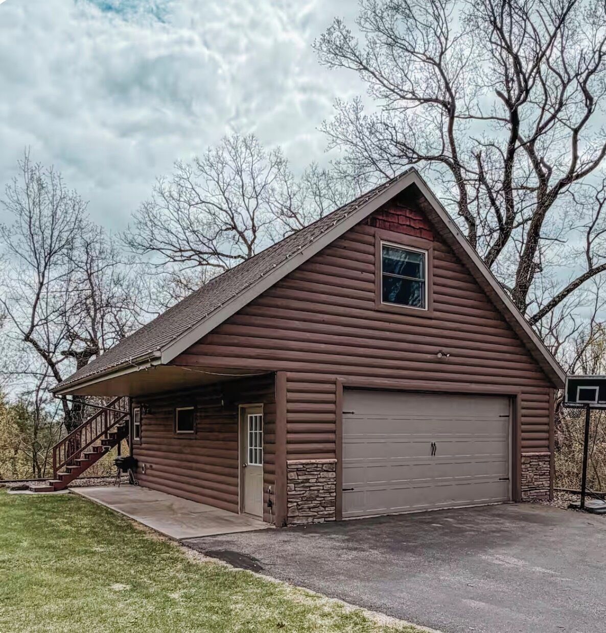 A log cabin with a garage, a covered porch, and a staircase leading to the entrance.