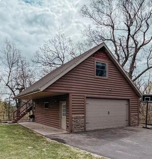 Une cabane en rondins avec un garage, une véranda et un escalier menant à l’entrée.