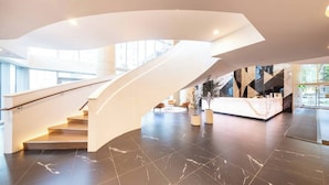 Eine moderne Lobby mit einer geschwungenen Treppe, Marmorböden und einem Empfangsbereich.