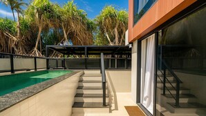 Une piscine dotée d’une balustrade en verre, d’une terrasse en bois et d’un escalier menant à un espace abrité.