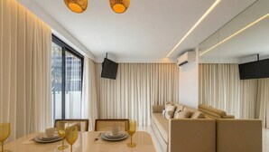 Un salon moderne avec un canapé, une table à manger dressée avec des assiettes et des verres, et un téléviseur fixé au mur.