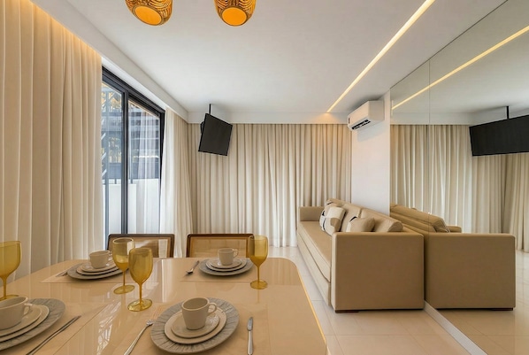 Una sala de estar moderna con un sofá, una mesa de comedor dispuesta con platos y vasos, y un televisor montado en la pared.