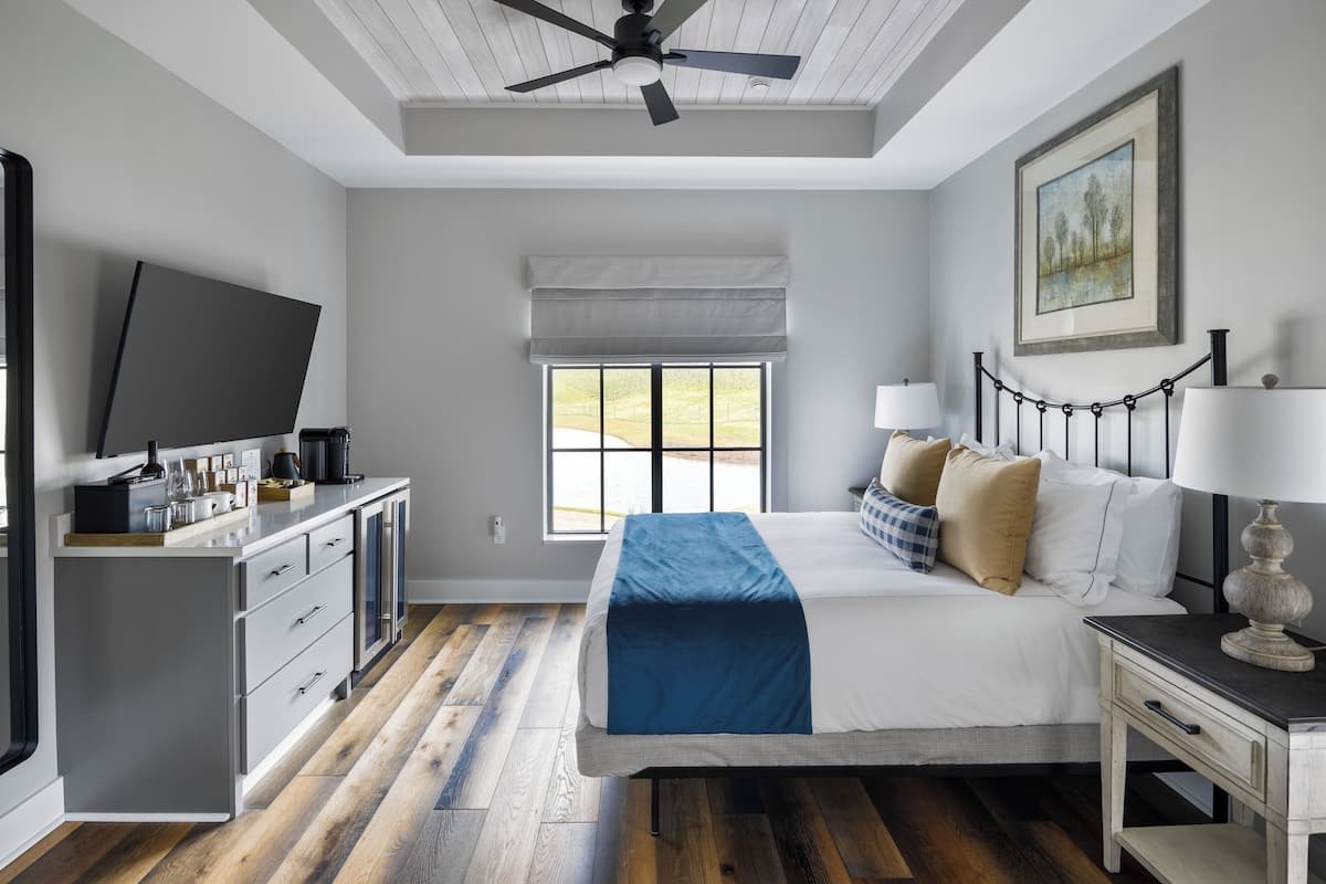 Un dormitorio con cama, mesita de noche, lámpara y televisor sobre un mueble.