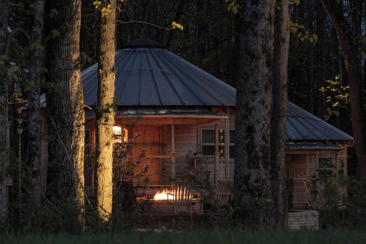 Una cabaña rodeada de árboles, con fuego encendido en la chimenea.