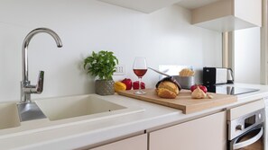 A modern kitchen with a stainless steel sink, a wooden countertop, a potted plant, a glass of red wine, a loaf of bread, and a garlic bulb. - Italianway - Bramante 29 (Milan)