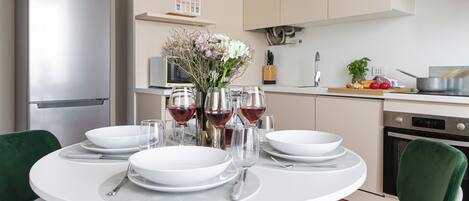 A modern kitchen with a dining table set for four, equipped with white plates, glasses, and cutlery.