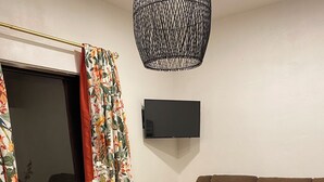 Un salon avec un canapé marron, une table ronde en bois accompagnée de deux tabourets, un téléviseur à écran plat fixé au mur et un tapis en peau de vache sur le sol.