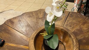 Une cuisine avec des meubles de couleur sombre, une cuisinière et un évier. On y trouve une statue de Bouddha sur le comptoir, une machine à café et un vase avec des fleurs blanches.