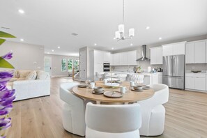 A modern kitchen with white cabinets, stainless steel appliances, and a dining area with white chairs and a round table. - Stylish Oasis - Riverwalk, Downtown, Armature (Tampa)