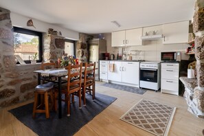 A kitchen with white cabinets, a stone wall, a dining table with chairs, and a view through a window.