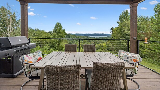 A covered outdoor patio with a wooden table and wicker chairs, overlooking a scenic landscape. - Grand Ole View on Center Hill Lake in Smithville, TN (Smithville)