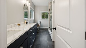 A modern bathroom with a large mirror, a vanity with drawers, a chair, and a glass shower door. - Grand Ole View on Center Hill Lake in Smithville, TN (Smithville)