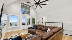 A spacious living room with a large brown leather sectional sofa, a ceiling fan, and a view of the ocean through large windows. - Grand Ole View on Center Hill Lake in Smithville, TN (Smithville)