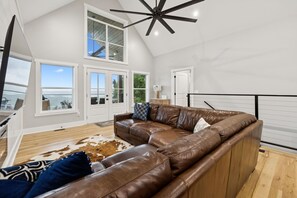 A spacious living room with a large brown leather sectional sofa, a ceiling fan, and a view of the ocean through large windows. - Grand Ole View on Center Hill Lake in Smithville, TN (Smithville)