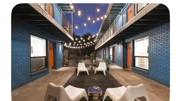 An outdoor seating area with a gravel floor, white plastic chairs, and a metal table. - Art-filled Cuban Studio 4 Creative Artsy Walkable Montrose Area. (Houston)