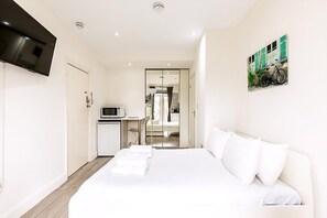 A hotel room with a bed, a TV, a desk with a microwave, and a door leading to a bathroom. - North End Hideaway (London)