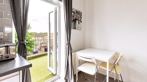 A kitchen with a toaster, a white table with chairs, and a view through a sliding glass door to a garden. - North End Hideaway (London)