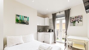 A bedroom with a bed, a small kitchenette, a dining area with a chair, and a balcony with a view. - North End Hideaway (London)