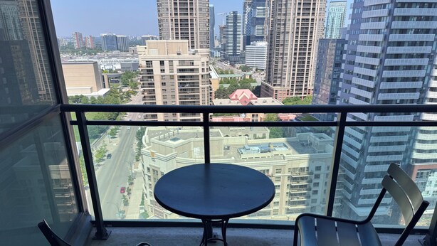 A balcony with a table and two chairs, overlooking a cityscape with modern buildings.
