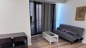 A modern living room with a grey sofa, a glass coffee table, and a wooden dining table with chairs.