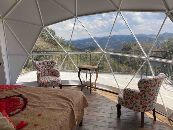 Una habitación en forma de cúpula con una cama, dos sillones florales y una mesita.