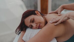 Eine Person liegt auf einem Bett mit einem weißen Kopfkissen und bekommt eine Massage.