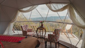 Ein Zeltraum mit Bett, floralen Stühlen, einem kleinen Tisch und Bergblick.