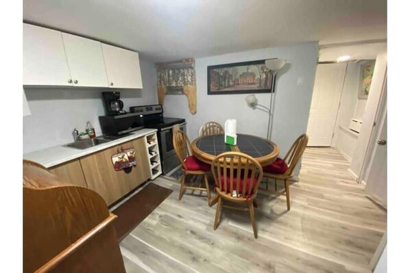 A compact kitchen with white cabinets, a stove, and a dining area with wooden chairs and a table.