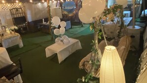 Een binnenterrras voor evenementen met tafels bedekt met witte tafelkleden, ballonnen en lichtslingers.