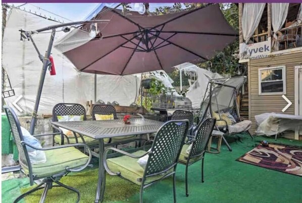 Un patio con mesa y sillas de metal, un paraguas grande y un área de estar techada.