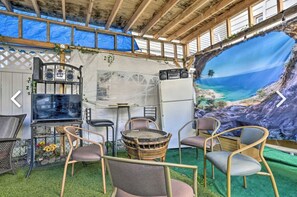 An outdoor seating area with a mural of a beach scene, a grill, and wicker chairs.