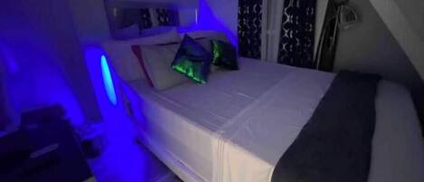 Un dormitorio con cama, almohadas y una mesita de noche.